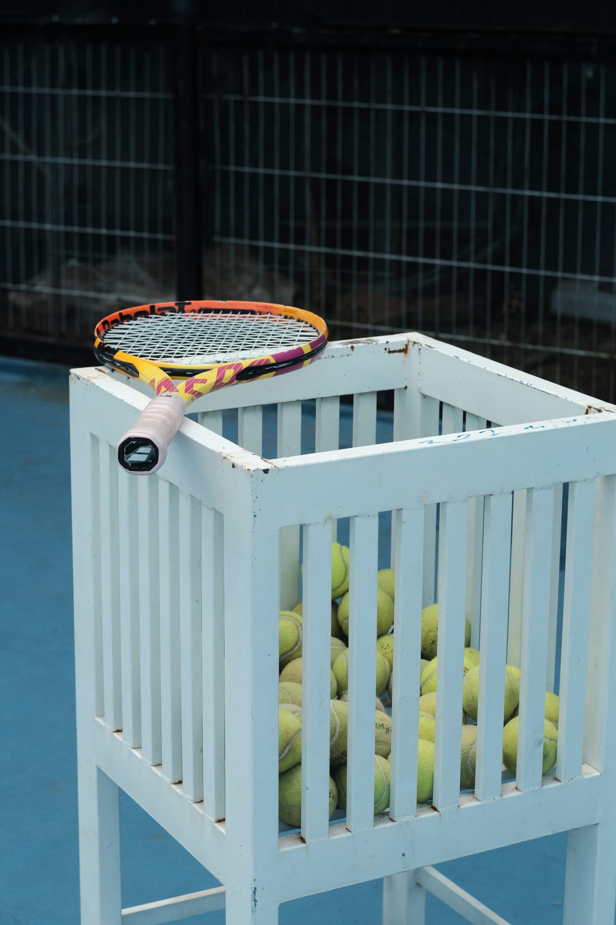 Padelschläger auf einem Ballkorb am Rand eines Courts hinter der Gitterwand