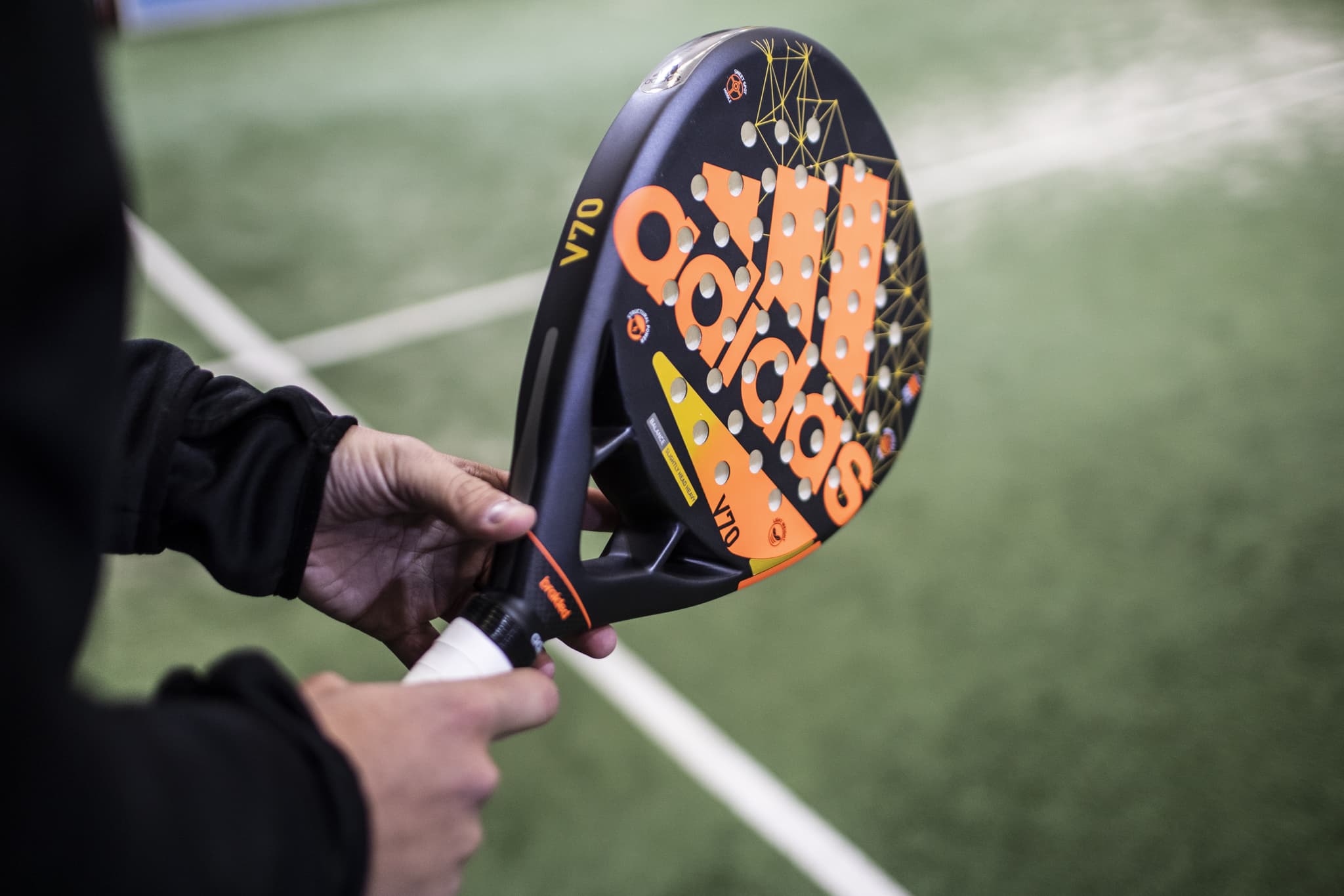 Spieler hält einen Padelschläger am Griff, im Hintergrund die Linien des Courts