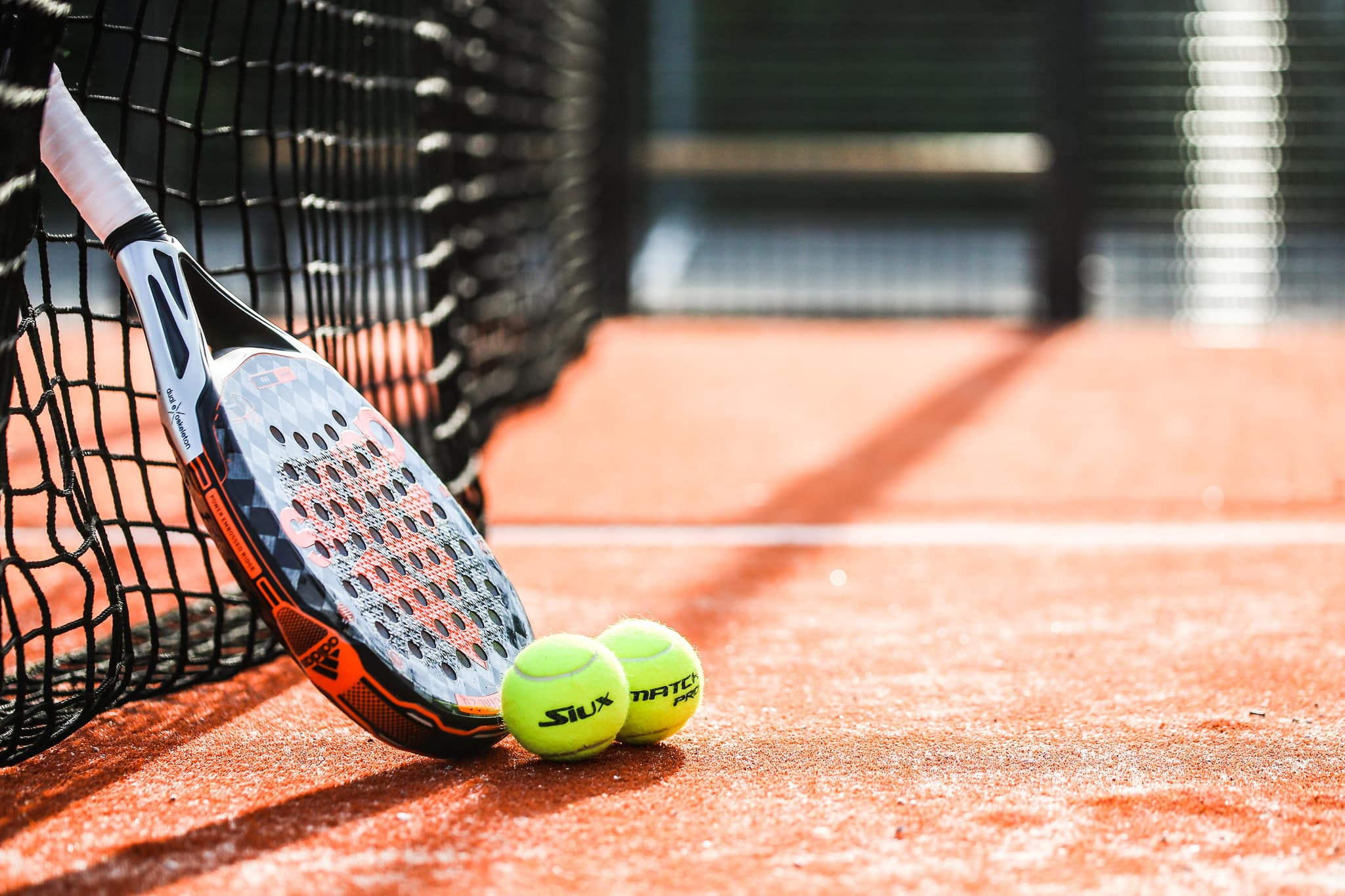 Zwei Padelschläger und Bälle am Netz eines Courts, dahinter die Glaswand