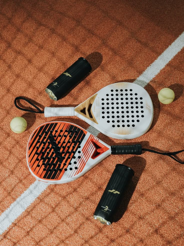 Zwei Padelschläger, Bälle und Griffbänder nebeneinander auf dem Boden ausgelegt